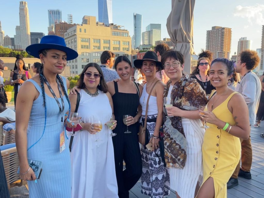 Six women of color stand on a rooftop deck, posing for a photo.