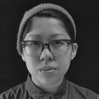 Tracy is an East Asian person with short dark hair tucked under a beanie and glasses.