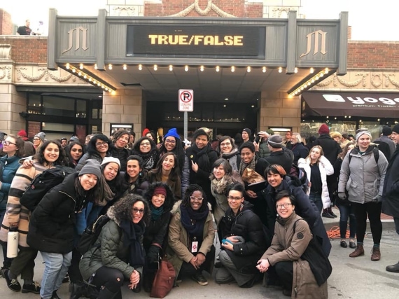 A large group of women and nonbinary people of color pose outside a movie theater with a marquee reading True/False.