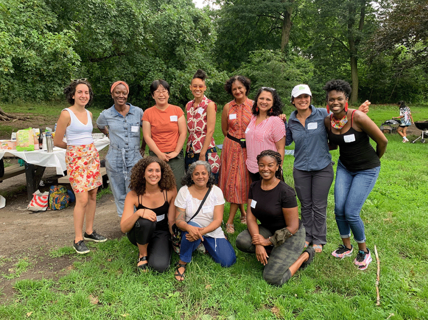 Eleven women and nonbinary people of color pose for a photo in a park.