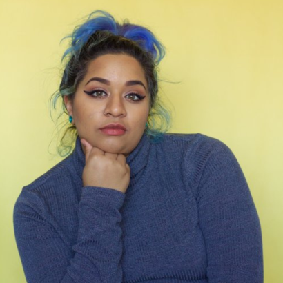 A multiracial Guyanese-American with hair tied up, wearing a blue turtleneck long sleeve.