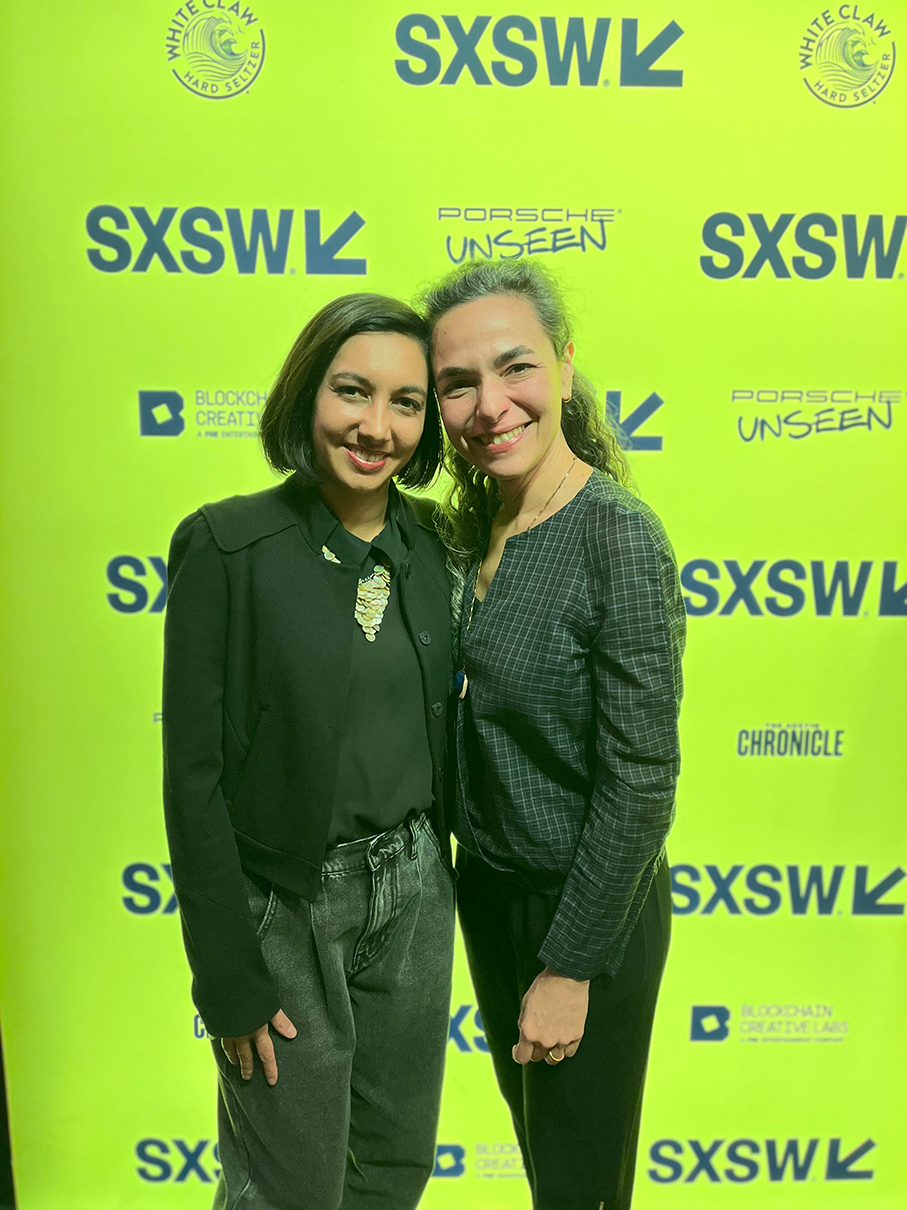 Two women posing before SXSW and Chronicle sponsor banner 