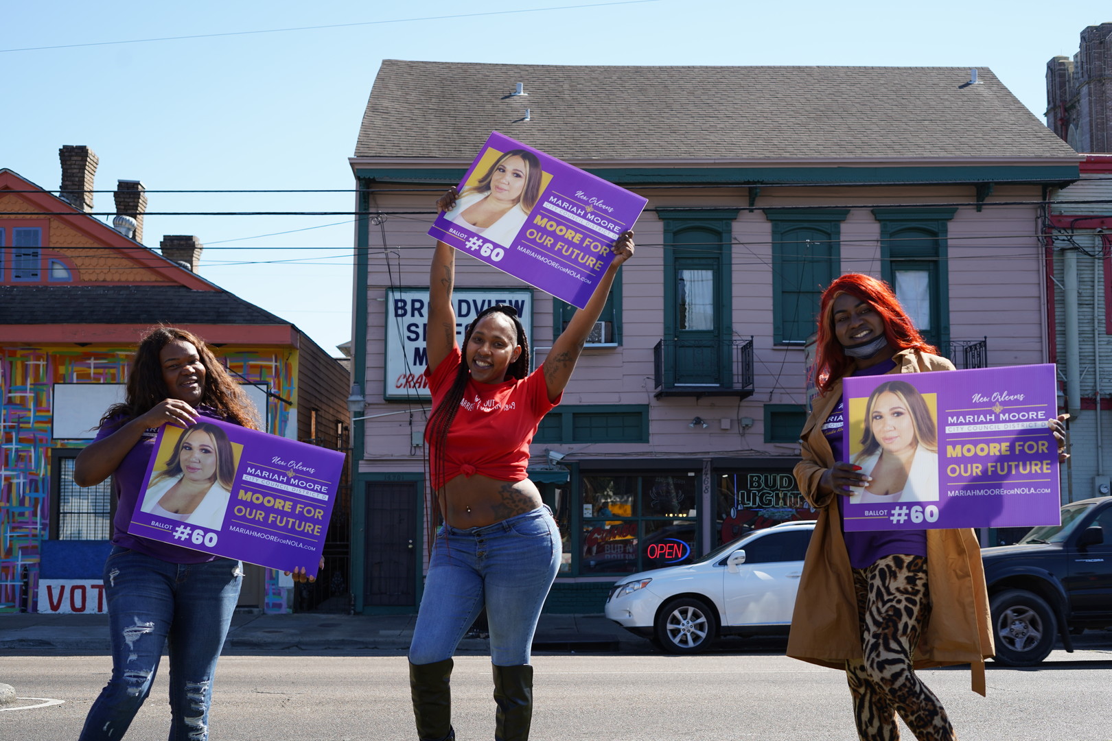 Three Black trans women hold up signs supporting Mariah Moore, a Black trans woman, in her run for city council.