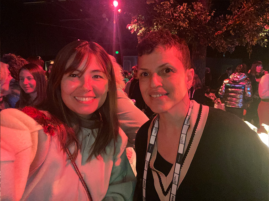 Michele, a Black woman with short curly hair and a lanyard, poses with an Asian woman for a selfie.