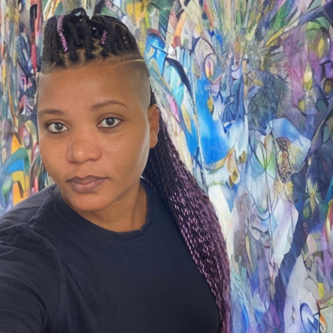In front of a large blue and purple mural, Zephrine, a Black Caribbean woman with the sides of her head shaved and long purple box braids on top.