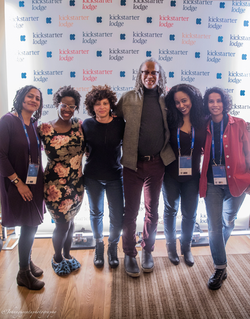 Six people of color with film festival badges around their neck pose in front of a Kickstarter step and repeat.