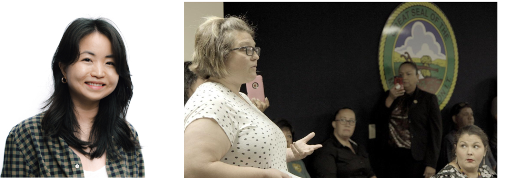 An East Asian woman in a blazer with medium length dark hair.  A blonde woman stands up to speak at a forum meeting.