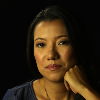 Juliana Sakae is a Japanese-Brazilian woman with long dark hair, resting her hand on her chin