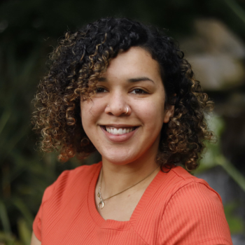 Kelsey is a light-skinned Black woman with curly brown hair and an orange shirt.