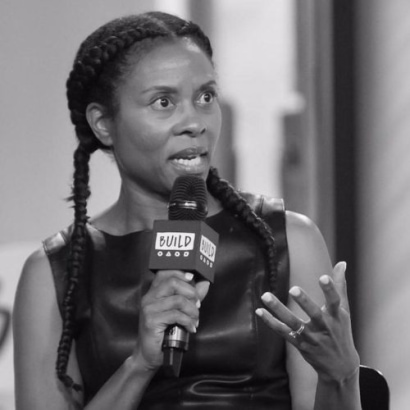 Luchina Fisher is a Black woman with long black braids and a sleeveless black dress.