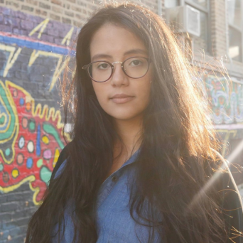 Miasarah Lai is a Chinese and Puerto Rican woman with long dark hair and round brown glasses, wearing a black jacket.