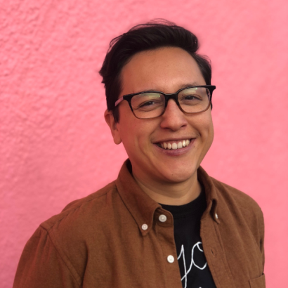 A mixed Mexican and Chinese American masc person wearing a brown jacket and glasses.