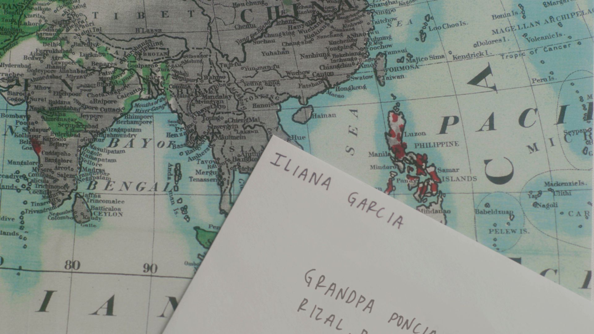 An envelope lays on top of a map of Southeast Asia, specifically over the Philippines. The envelope is addressed to Grandpa Poncio, from Iliana Garcia. 